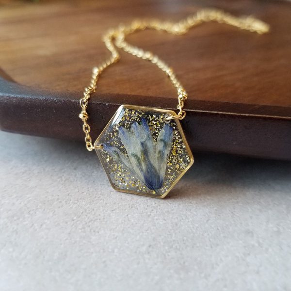 Add a touch of whimsy to your wardrobe with this unique one of a kind dried pressed wildflower resin necklace that has been made with high quality resin and sprinkled with gold glitter.